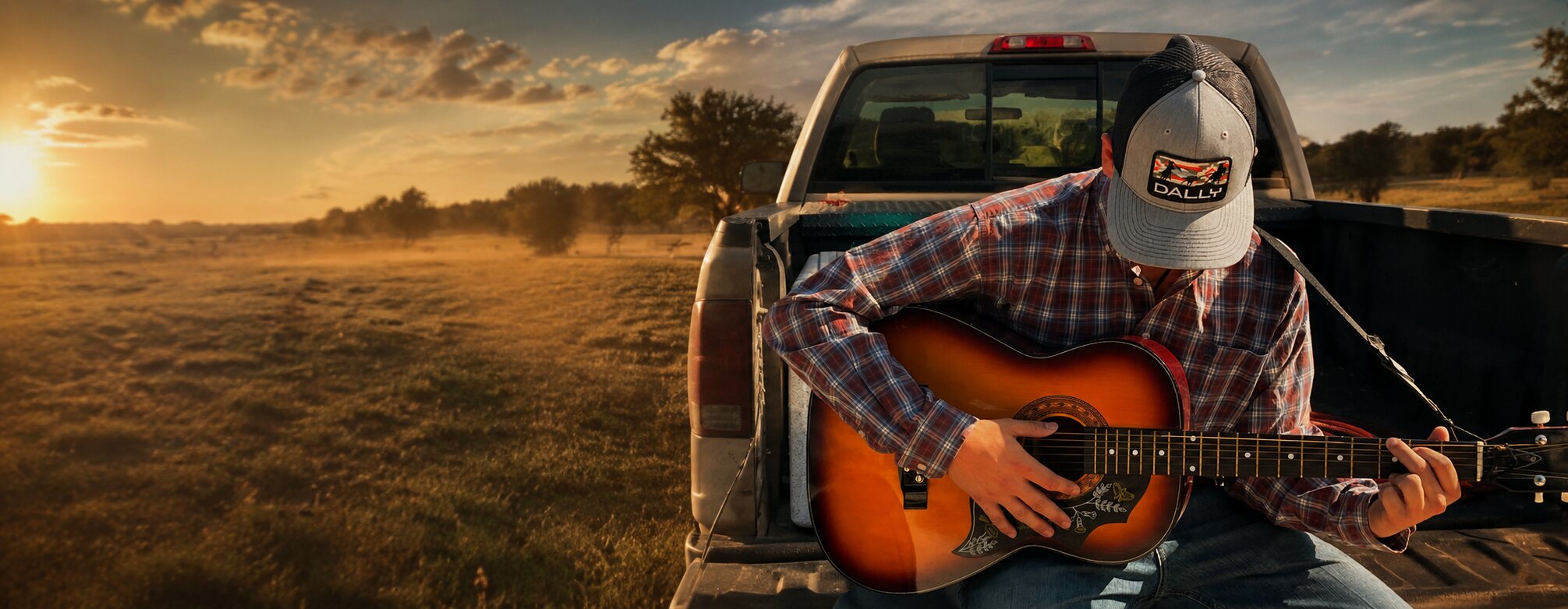Cowboy wearing a Dally Up cap beside a pickup at sunset